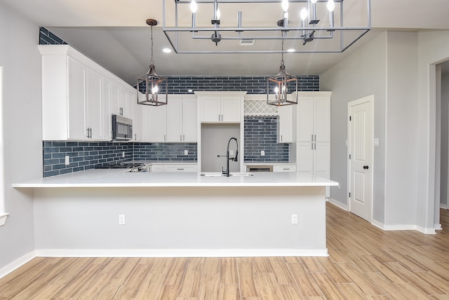 kitchen featuring sink, decorative light fixtures, light hardwood / wood-style flooring, kitchen peninsula, and white cabinets