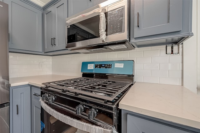 kitchen featuring tasteful backsplash, gray cabinetry, light stone countertops, and stainless steel appliances