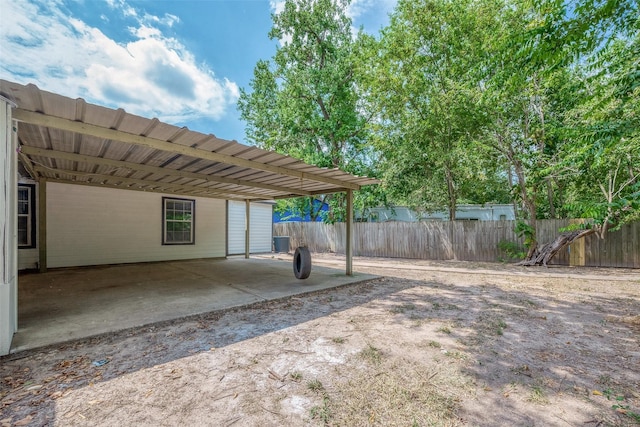 view of yard featuring an attached carport, driveway, central AC, and fence