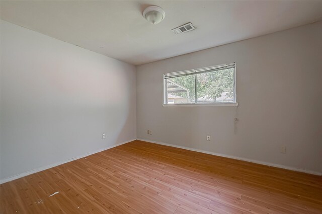 empty room featuring light wood-type flooring, visible vents, and baseboards