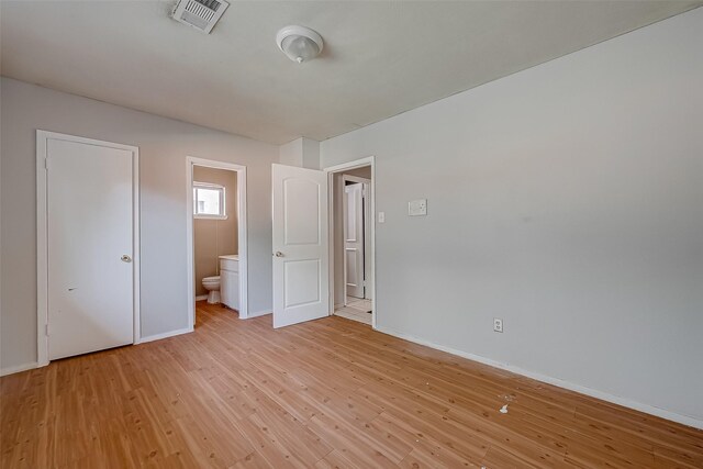 unfurnished bedroom featuring light wood-style flooring, connected bathroom, visible vents, and baseboards