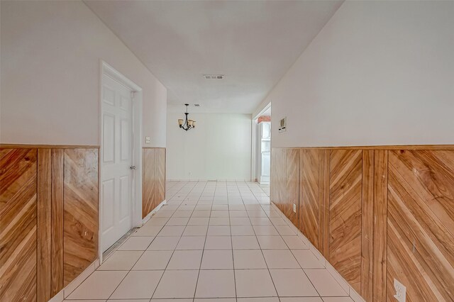 hallway with a wainscoted wall, light tile patterned floors, wood walls, and visible vents