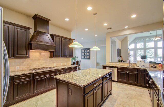 kitchen with pendant lighting, custom exhaust hood, appliances with stainless steel finishes, light stone counters, and light tile patterned floors