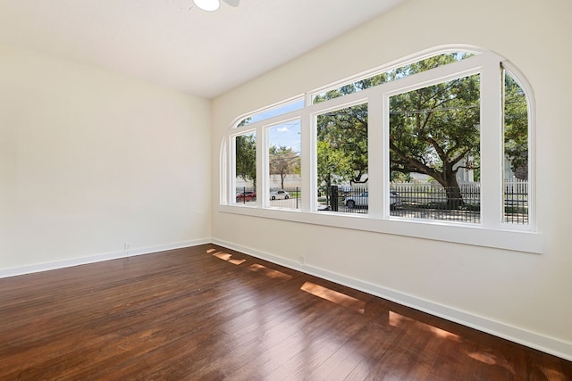 unfurnished room featuring baseboards, a ceiling fan, and dark wood finished floors