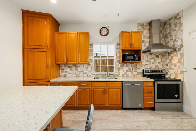 kitchen featuring wall chimney exhaust hood, brown cabinetry, decorative backsplash, stainless steel appliances, and a sink