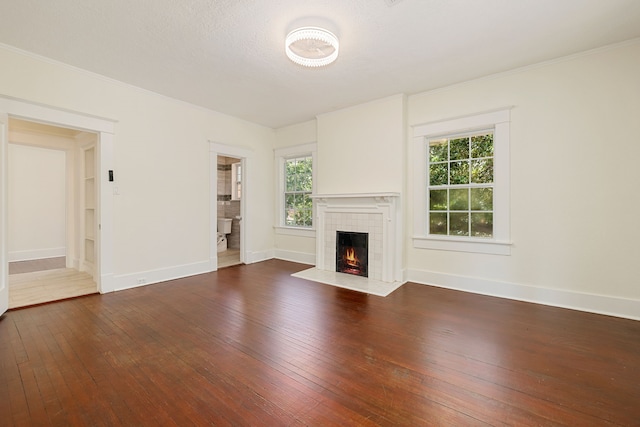 unfurnished living room with hardwood / wood-style floors, a tiled fireplace, ornamental molding, and baseboards