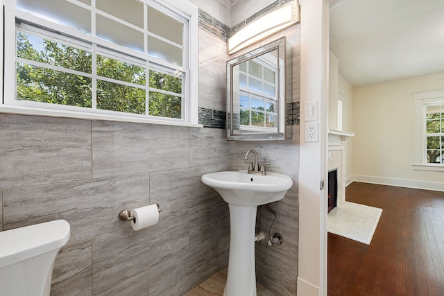 half bath with a tiled fireplace, wood-type flooring, toilet, and baseboards