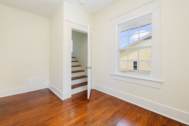empty room featuring visible vents, baseboards, stairway, and wood finished floors