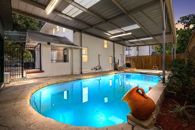 pool at dusk featuring fence, a patio, and an indoor pool