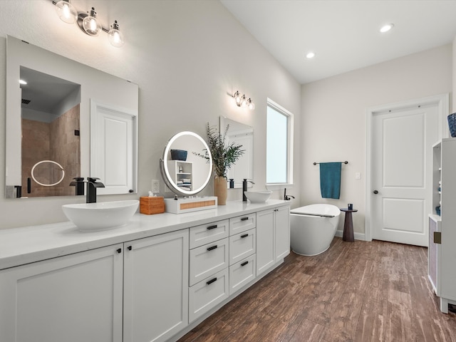 full bathroom with a soaking tub, wood finished floors, a sink, and double vanity