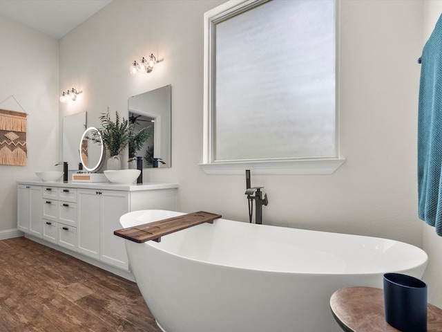 full bathroom featuring double vanity, a sink, a freestanding bath, and wood finished floors