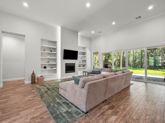 living area with ornamental molding, visible vents, a fireplace, and wood finished floors