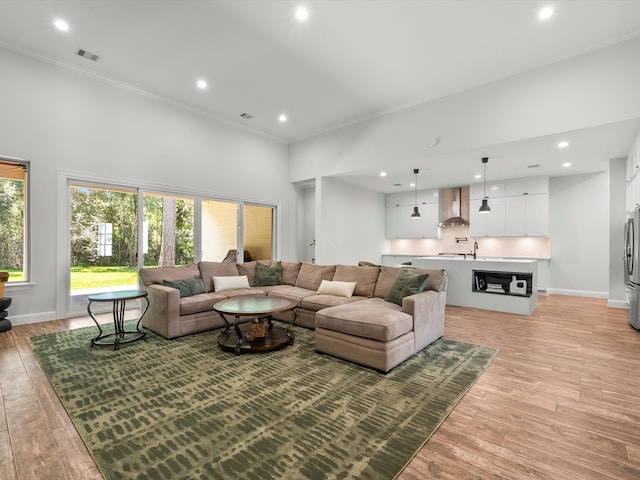 living room featuring light wood-style floors, baseboards, visible vents, and crown molding