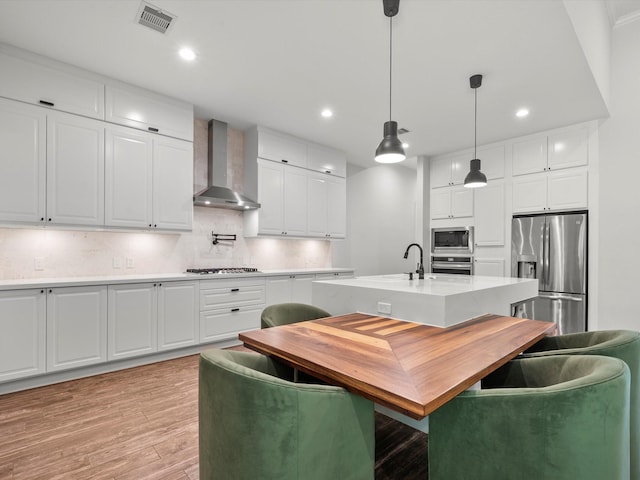 kitchen with stainless steel appliances, visible vents, light countertops, wall chimney range hood, and light wood finished floors