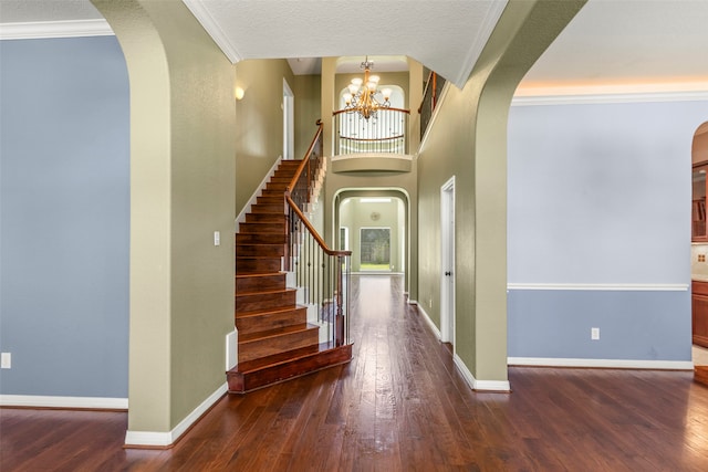 foyer with dark wood-type flooring, ornamental molding, a textured ceiling, and a chandelier