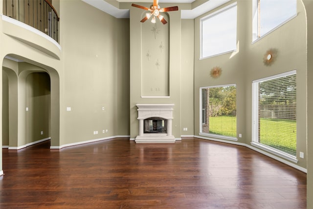 unfurnished living room featuring a wealth of natural light, ceiling fan, hardwood / wood-style flooring, and a towering ceiling