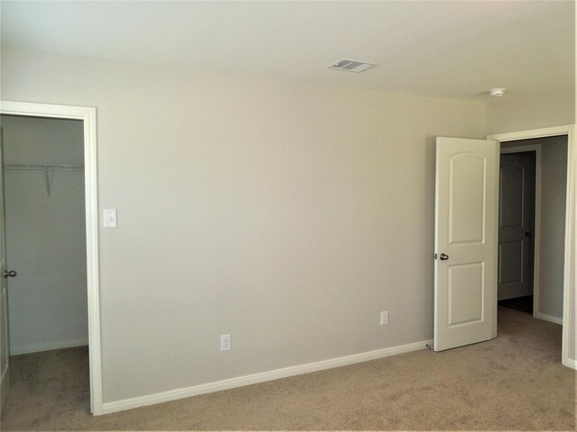 unfurnished bedroom featuring a spacious closet, a closet, and light carpet