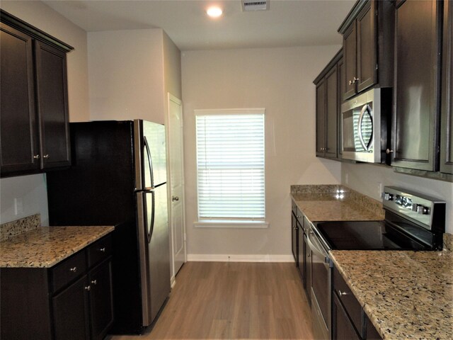 kitchen with light wood-type flooring, dark brown cabinetry, stainless steel appliances, and light stone countertops