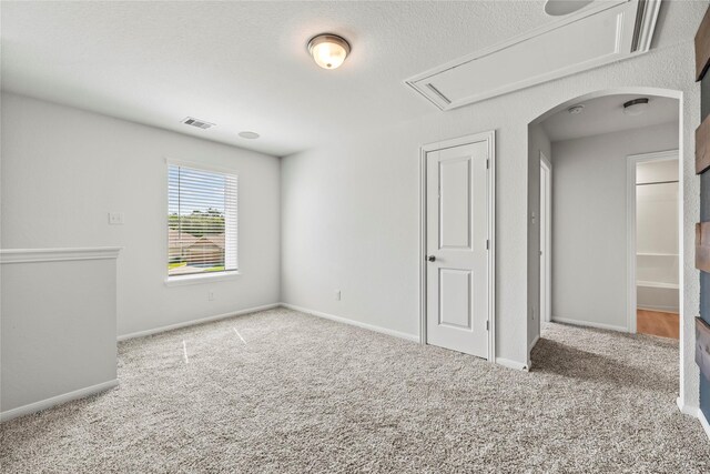 empty room with carpet, visible vents, arched walkways, and baseboards