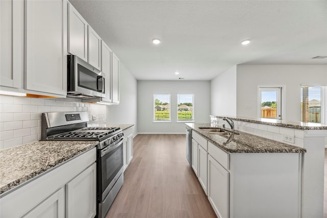 kitchen featuring stone counters, stainless steel appliances, light wood-style flooring, decorative backsplash, and a sink