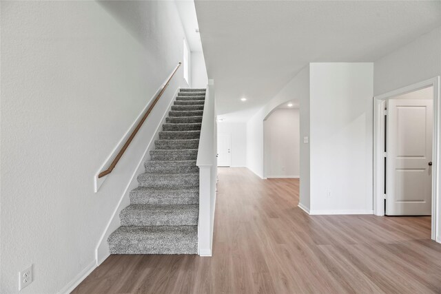 staircase with arched walkways, recessed lighting, baseboards, and wood finished floors