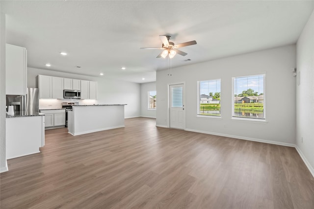 unfurnished living room featuring a healthy amount of sunlight, light wood finished floors, ceiling fan, and baseboards