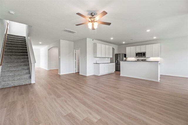 unfurnished living room featuring visible vents, ceiling fan, stairway, and light wood finished floors