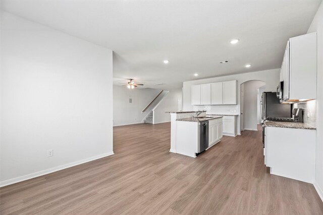 kitchen with arched walkways, ceiling fan, backsplash, and light wood-style flooring