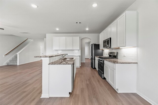 kitchen with light wood-type flooring, arched walkways, stainless steel appliances, and a sink