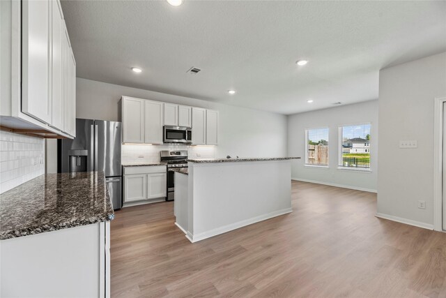 kitchen with white cabinets, light wood-style floors, appliances with stainless steel finishes, and decorative backsplash