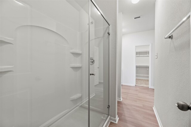 bathroom featuring wood finished floors, a shower stall, visible vents, and baseboards