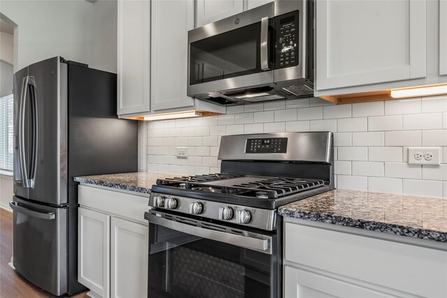 kitchen featuring white cabinetry, tasteful backsplash, appliances with stainless steel finishes, and dark stone countertops