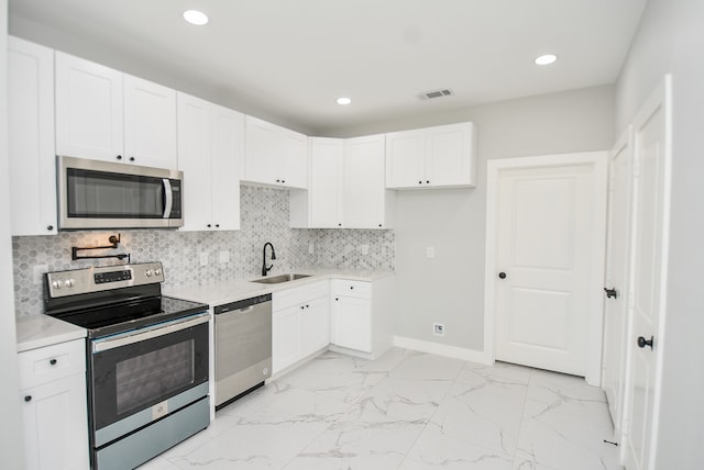 kitchen with backsplash, sink, light tile patterned floors, appliances with stainless steel finishes, and white cabinetry