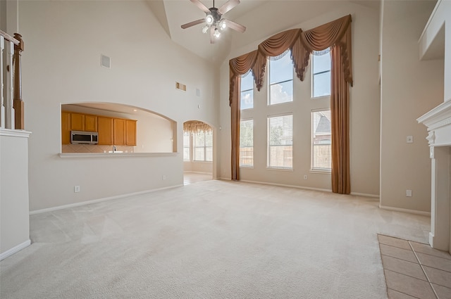 unfurnished living room with ceiling fan, a towering ceiling, and light carpet