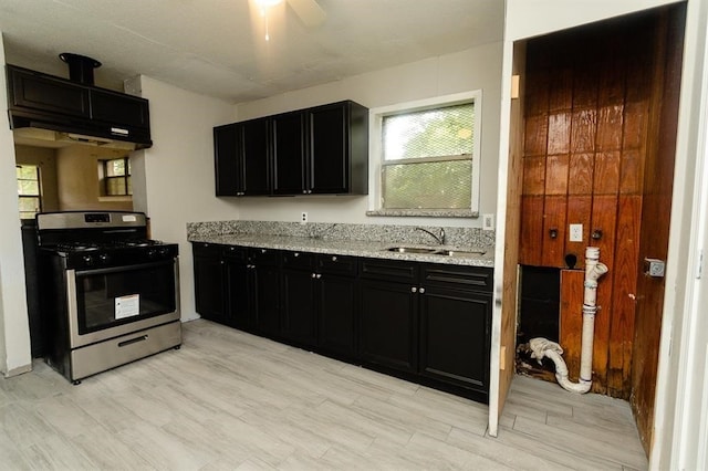 kitchen with sink, stainless steel gas range oven, custom exhaust hood, light stone counters, and ceiling fan