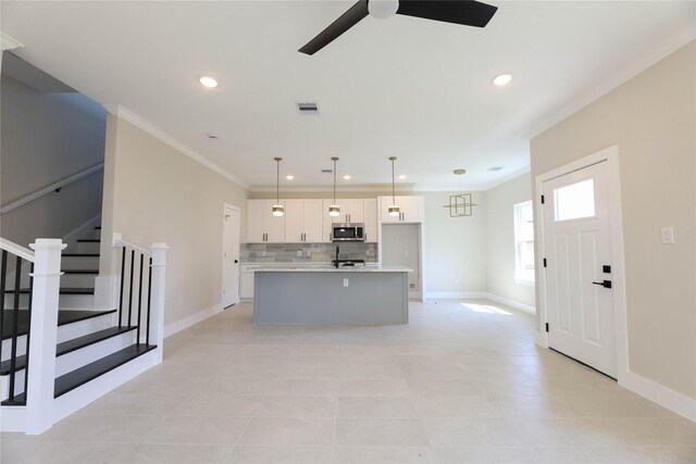 kitchen with pendant lighting, tasteful backsplash, an island with sink, white cabinetry, and crown molding