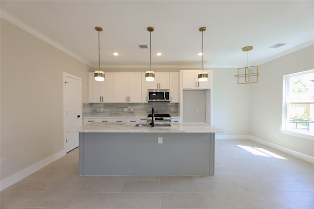 kitchen featuring hanging light fixtures, sink, a center island with sink, backsplash, and white cabinetry