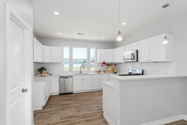 kitchen featuring visible vents, a sink, stainless steel appliances, light wood-style floors, and a peninsula