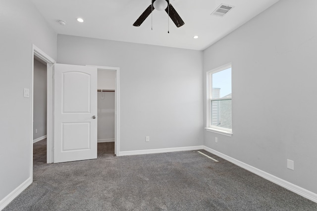 unfurnished bedroom with dark carpet, a closet, ceiling fan, and a walk in closet