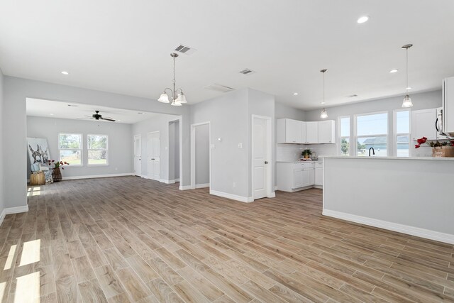 unfurnished living room featuring ceiling fan with notable chandelier and light hardwood / wood-style floors