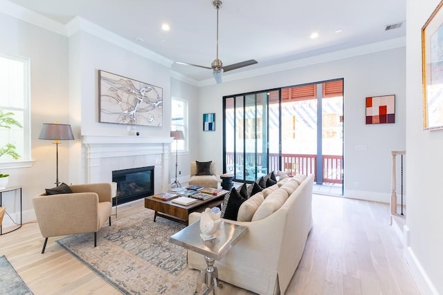 living room featuring ceiling fan, light hardwood / wood-style floors, ornamental molding, and a tiled fireplace