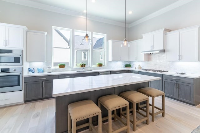 kitchen featuring stainless steel appliances, light hardwood / wood-style flooring, decorative backsplash, white cabinets, and hanging light fixtures