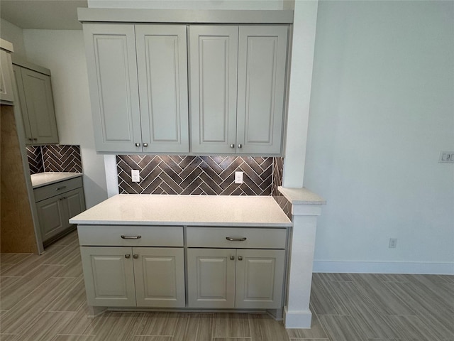 kitchen with gray cabinetry, baseboards, light countertops, backsplash, and wood tiled floor