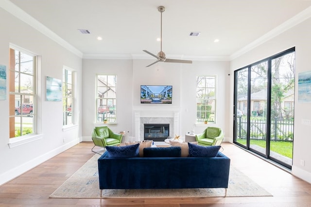 living room with ceiling fan, light wood-type flooring, crown molding, and a high end fireplace