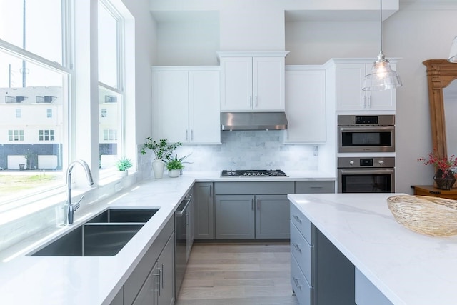 kitchen featuring sink, light wood-type flooring, appliances with stainless steel finishes, tasteful backsplash, and gray cabinetry