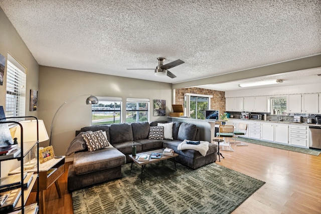 living room with ceiling fan, light wood-type flooring, and a textured ceiling