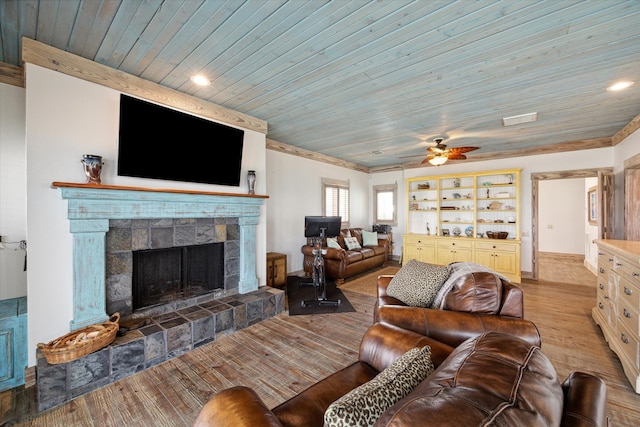 living room featuring a tiled fireplace, ceiling fan, wooden ceiling, light hardwood / wood-style flooring, and built in features