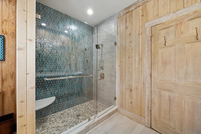 bathroom with a shower with door, wooden walls, and hardwood / wood-style floors