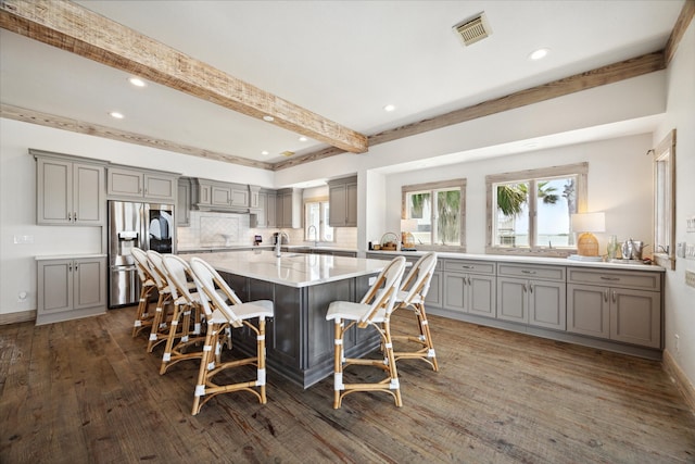 kitchen with dark hardwood / wood-style floors, beamed ceiling, stainless steel refrigerator with ice dispenser, a breakfast bar, and a center island