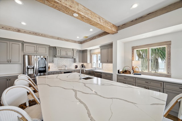 kitchen with beamed ceiling, a healthy amount of sunlight, light stone counters, and a breakfast bar area